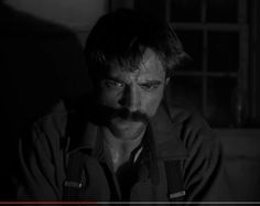 a man with a moustache stares at the camera in a dark room,