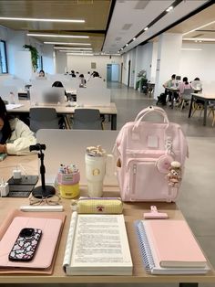 a woman sitting at a table with a pink backpack and other items on it, in an office setting