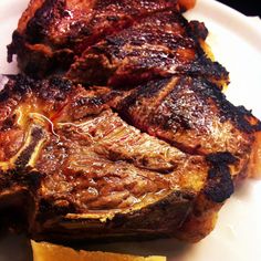 some meat is sitting on a white plate with orange slices around it and another piece has been cut into pieces