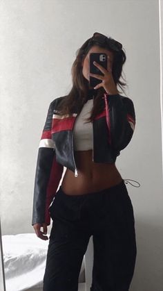 a woman taking a selfie with her cell phone in front of a mirror wearing black pants and a leather jacket