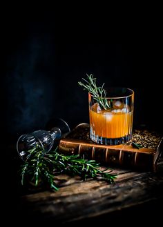 a glass filled with liquid sitting on top of a wooden table next to an olive branch