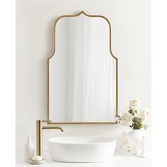 a white sink sitting under a large mirror next to a vase with flowers on it