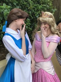 two women dressed up as princesses talking to each other in front of some bushes