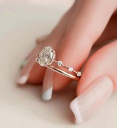 a woman's hand holding a ring with a diamond on it and white nails