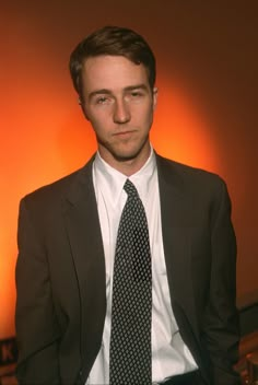 a man in a suit and tie posing for the camera with an orange light behind him