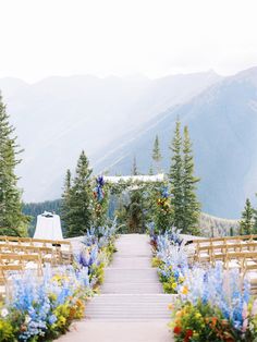 an outdoor ceremony setup with wooden chairs and flowers on the aisle leading up to the altar