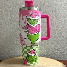 a pink and green travel mug sitting on top of a wooden table next to a white wall