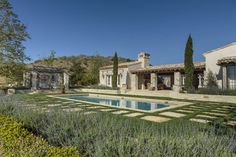 an outdoor swimming pool surrounded by greenery and lavender bushes in front of a house