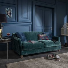 a living room with blue walls and a green velvet couch in the middle, surrounded by other furniture