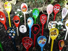 there are many different colored spoons on the ground in front of some plants and flowers