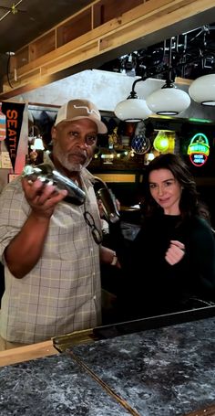 a man standing behind a counter with a woman looking at the camera and holding something in his hand