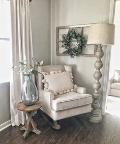 a white chair sitting next to a lamp on top of a wooden table in front of a window