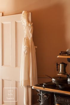 a white dress hanging on the wall next to an old fashioned stove top and oven