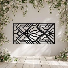 an abstract metal art piece hanging on the wall next to white flowers and greenery