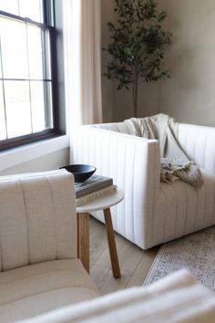 a living room with two white chairs and a coffee table in front of a window