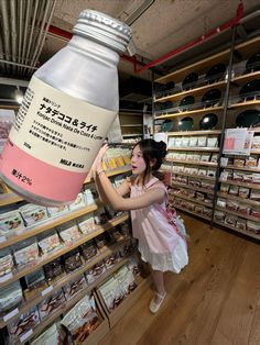 a woman in a store looking at food on shelves and reaching up to grab something out of the jar