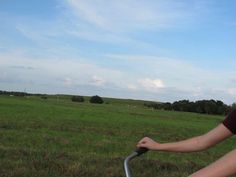 a woman riding on the back of a bike through a lush green field under a blue sky