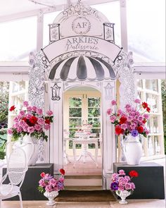 a white gazebo with pink and red flowers on the front porch, surrounded by chairs