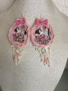 two pink earrings with pictures on them are hanging from a mannequin's torso