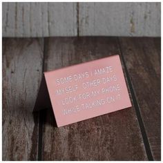 a pink note with some words on it sitting on top of a wooden table in front of a wall