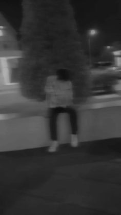 black and white photograph of person sitting on wall at night with street lights in background