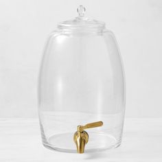 a glass jar with a gold faucet on the side and a white background