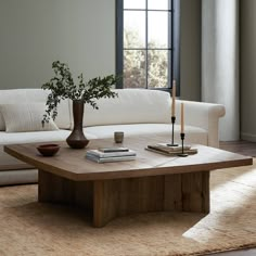 a living room with a couch, coffee table and vase on the floor in front of a window