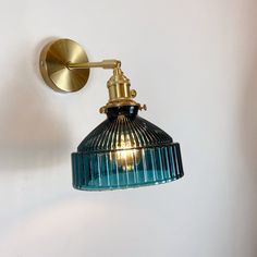 a wall light with a blue glass shade on it's side and a gold metal arm