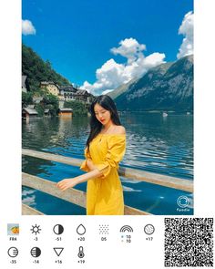 a woman in a yellow dress standing on a pier next to the water and mountains