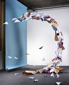 paper birds are flying in the air near a blue wall and an arch made out of origami