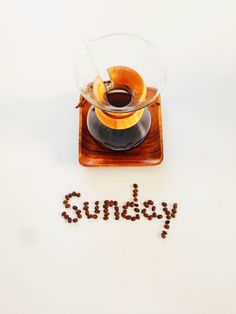 the word sunday spelled with coffee beans in front of a cup of coffee on a saucer