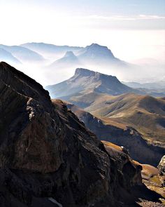 a mountain range with mountains in the distance and clouds hovering over it's top