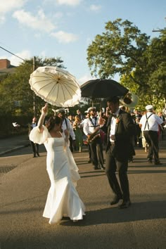 a bride and groom walking down the street with umbrellas in their hands as people look on