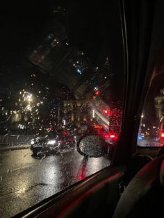 the view from inside a car looking at traffic on a rainy night with red and blue lights