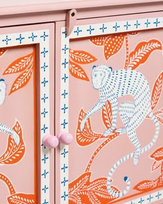 an orange and blue painted cabinet with two pink knobs on the front, and a monkey design on the back