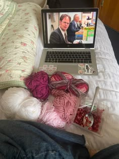 a laptop computer sitting on top of a bed next to yarn and crochet