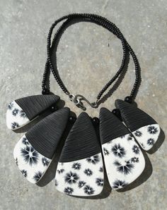 a black and white necklace with five large pendants on it's sides, sitting on a concrete surface