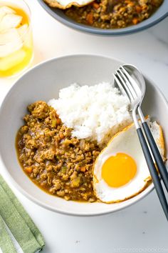 two bowls filled with rice and eggs on top of a white table next to silverware