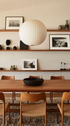 a dining room table with chairs and pictures on the wall above it, along with hanging lights