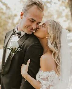 a bride and groom kissing each other in front of a tree on their wedding day