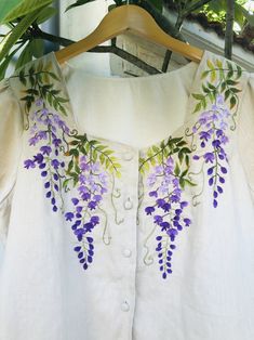 a white shirt with purple flowers on it and green leaves hanging from the collarline