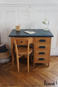 a desk with a chair and a lamp on top of it in front of a white wall