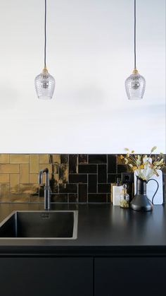 three lights hanging from the ceiling above a sink in a black kitchen with gold tiles