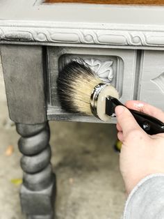 a person using a brush to paint an old table with grey paint and silver drawers