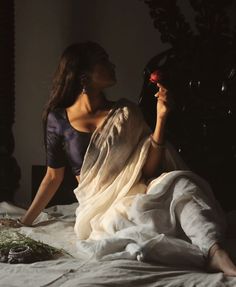 a woman sitting on top of a bed holding a red flower in her right hand