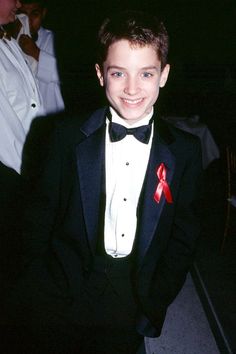 a young boy in a tuxedo smiles at the camera while wearing a red bow tie