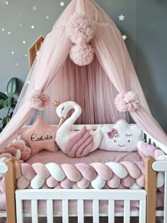 a pink and white baby crib with a swan on it's pillow, stuffed animals and pillows