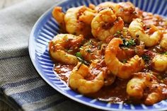 a blue plate filled with cooked shrimp and sauce on top of a table next to a napkin