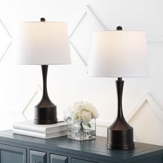 two lamps sitting on top of a dresser next to a vase with flowers in it