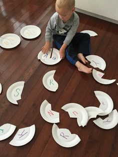 a young boy sitting on the floor with paper plates in front of him that have numbers written on them